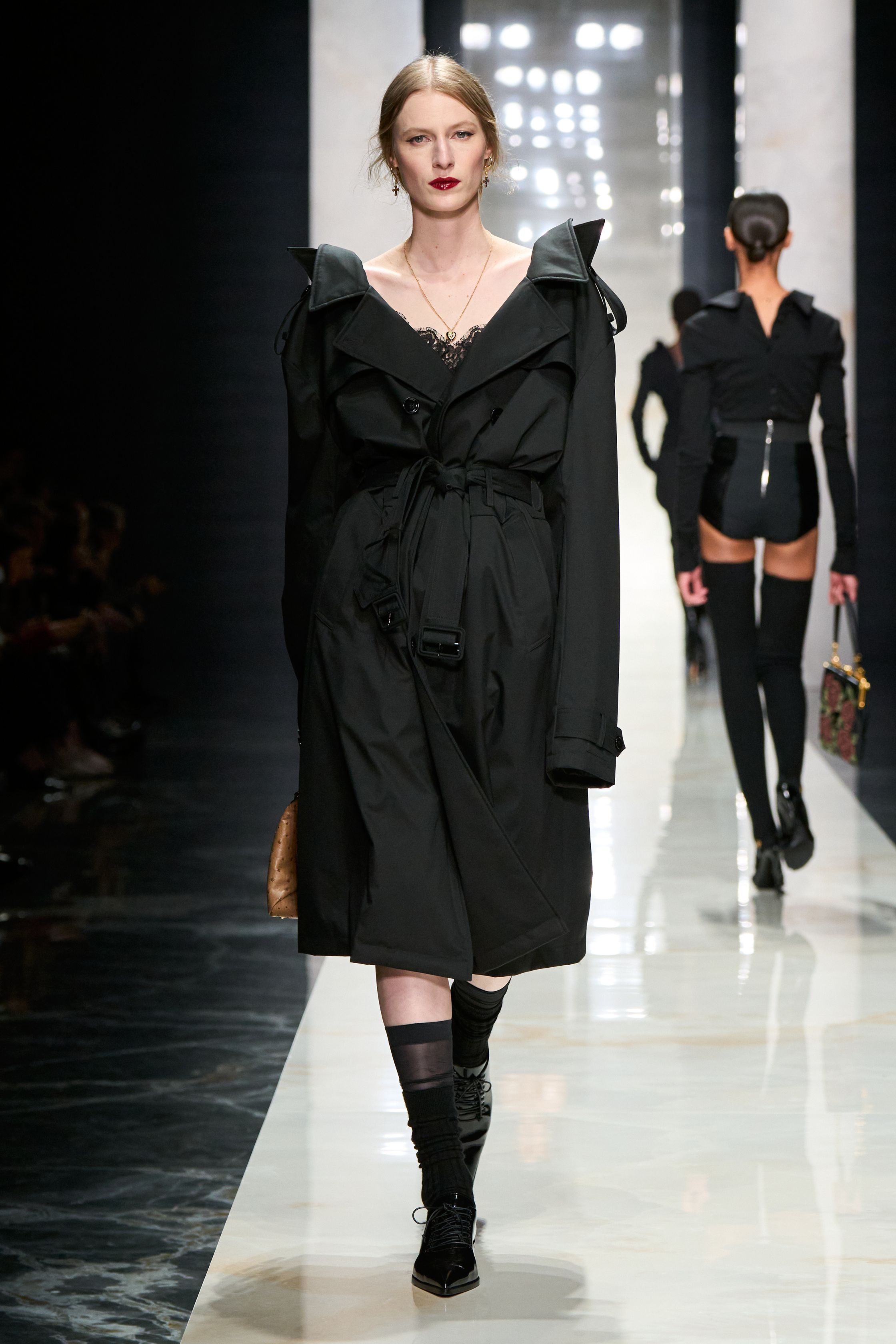 Dolce & Gabbana在本季回归品牌标志性的性感意大利美学，通过黑色蕾丝、修身西装与透视礼服塑造极具戏剧张力的女性形象。系列以黑色为核心色调，结合紧身胸衣结构、透明蕾丝裙与宽肩西装，形成刚柔并济的视觉语言。皮草外套与复古帽饰则增添奢华氛围，使整体造型在性感与优雅之间保持平衡，呈现出典型的意大利电影般的华丽气质-顽石频道趋势研究
